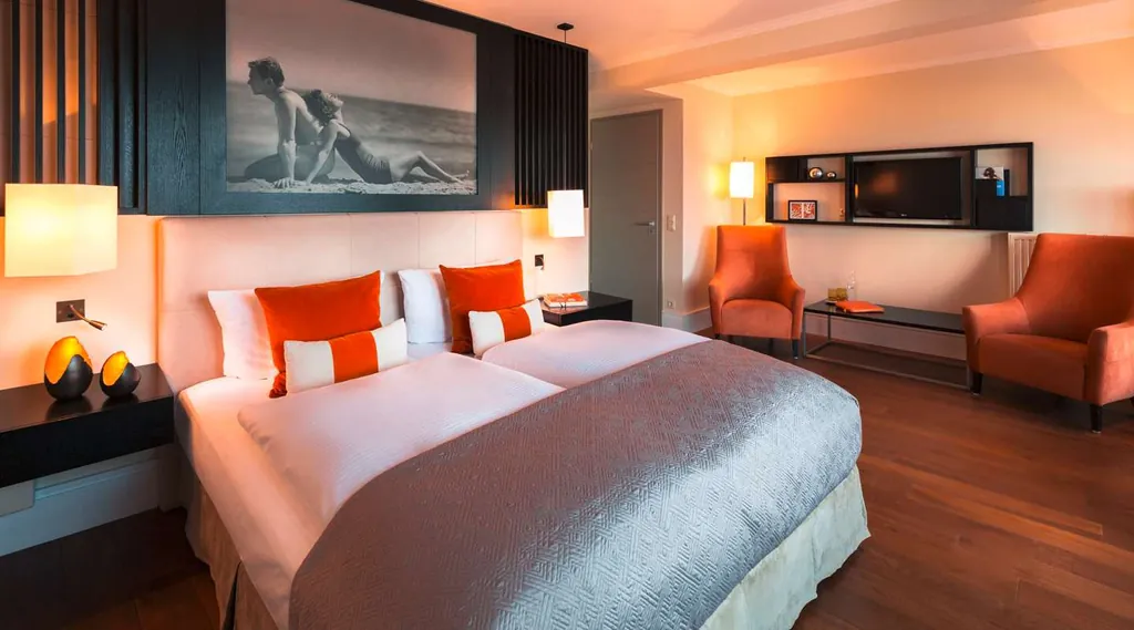 Doppelzimmer mit orangen Sesseln und Schwarz/Weiß-Fotografie über dem Bett im Strandhotel Ostseeblick