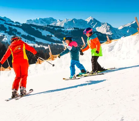 Zwei Kinder üben zusammen mit Lehrer das Skifahren