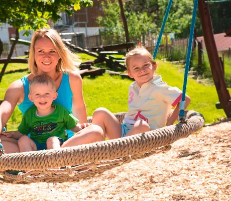 Junge Mutter sitzt mit ihren beiden Kindern in großer Hängeschaukel