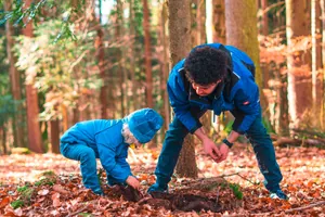 Mann und Kind spielen am Waldboden im Waldkinder-Club im Familienhotel Landhaus zur Ohe