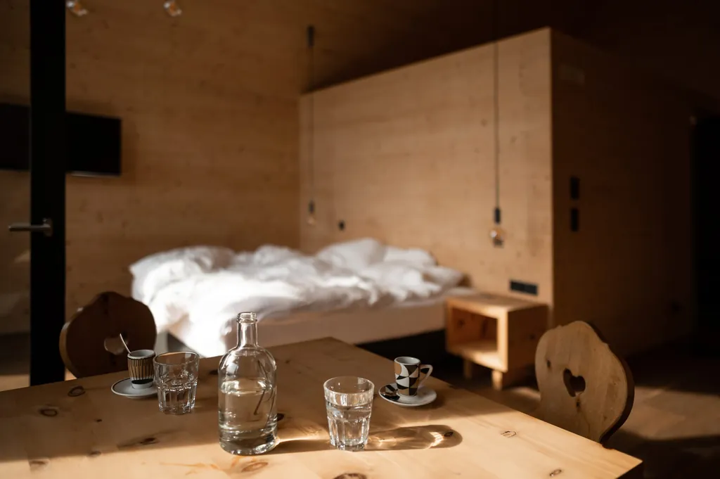 Holztisch in Hotelzimmer mit Wasser und Kaffee, Bett mit weißen Decken im Hintergrund