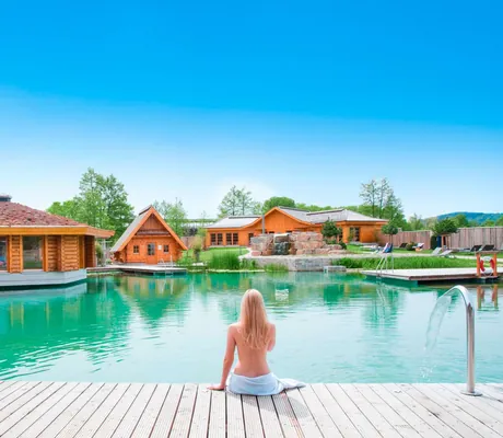 Frau sitzt am grünen Teich mit Holzhütten im