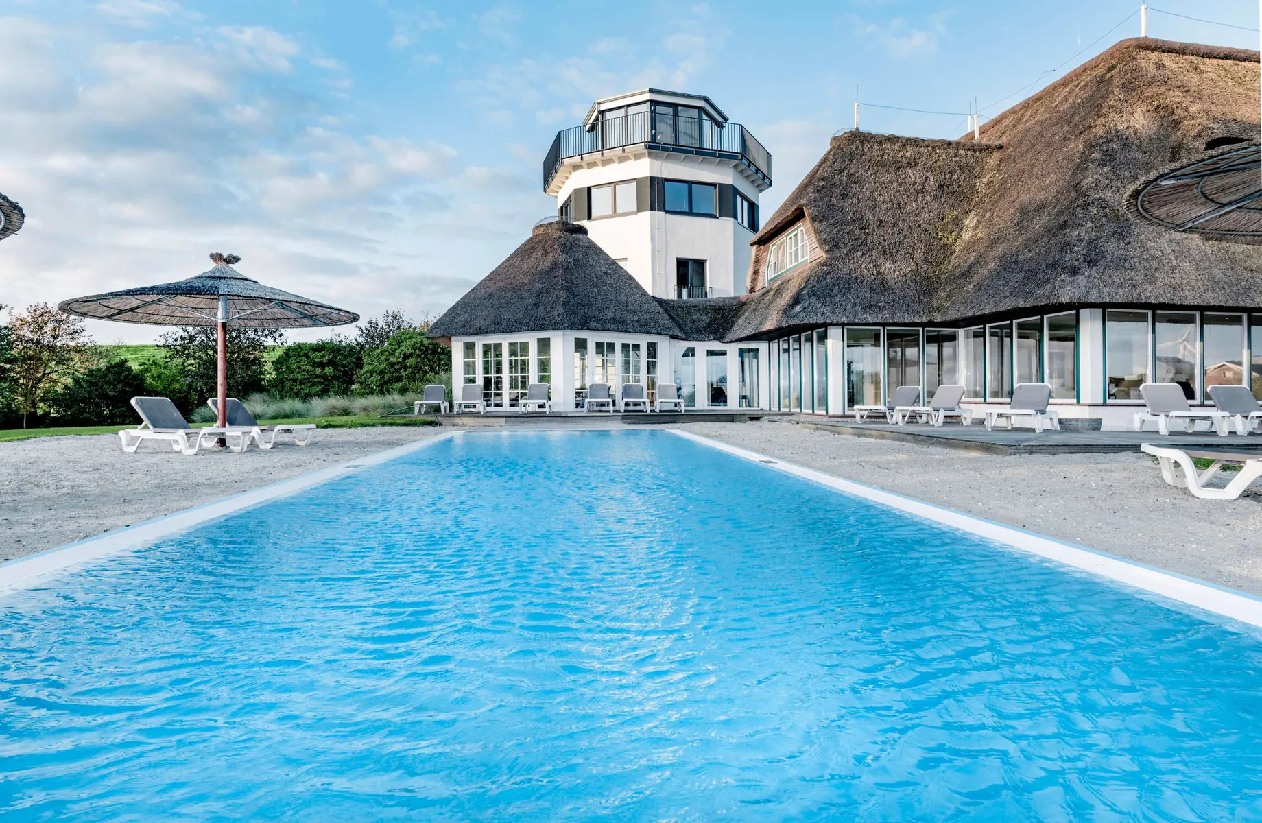 Blick über den Außenpool auf das reetgedeckte Hotel Lundenbergsand