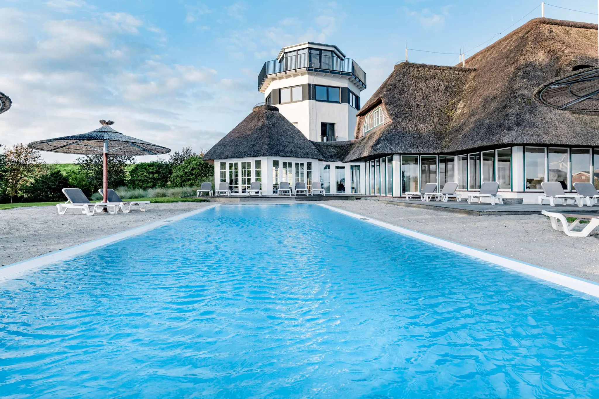 Blick über den Außenpool auf das reetgedeckte Hotel Lundenbergsand