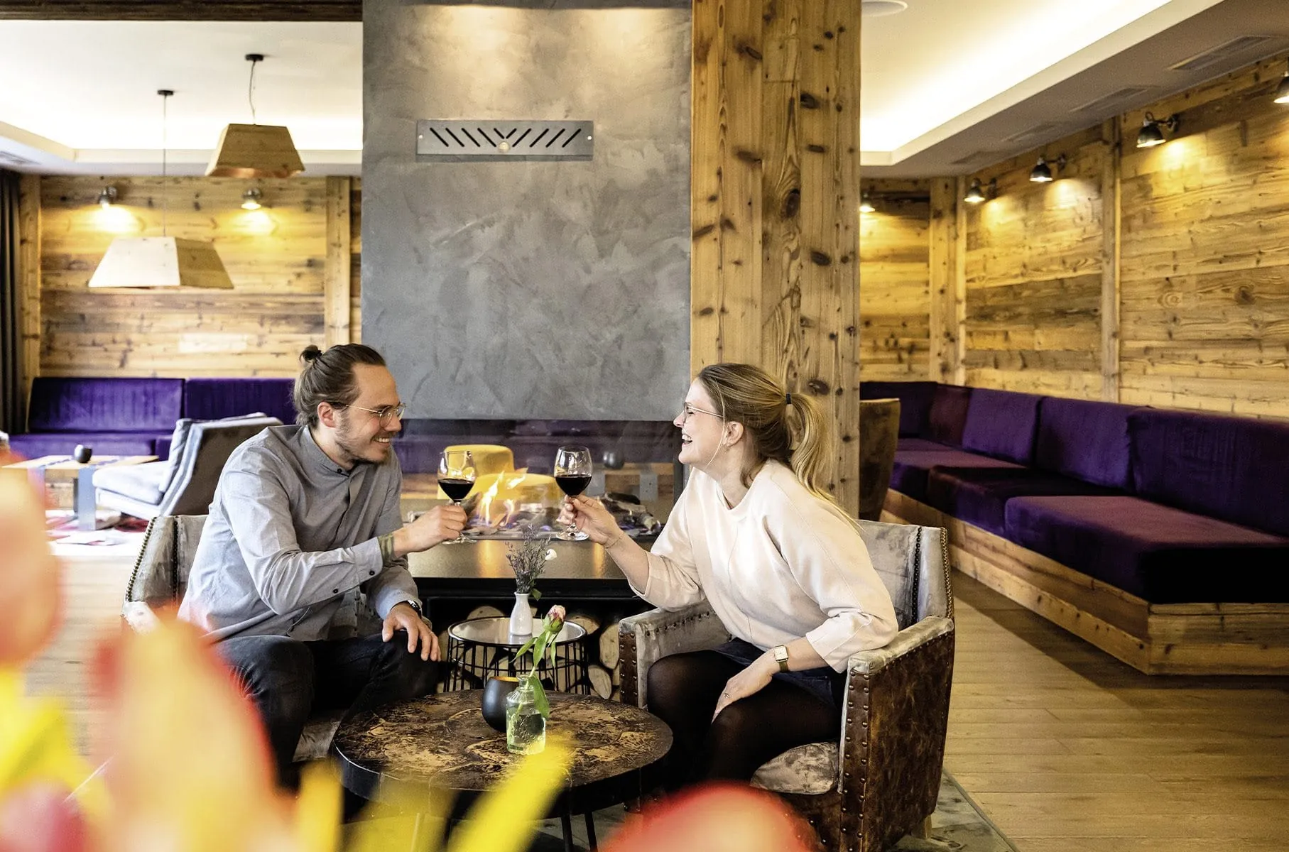 Eltern sto&szlig;en in der gem&uuml;tlich eingerichteten Lounge im Familotel Sonnenpark mit Weingl&auml;sern an