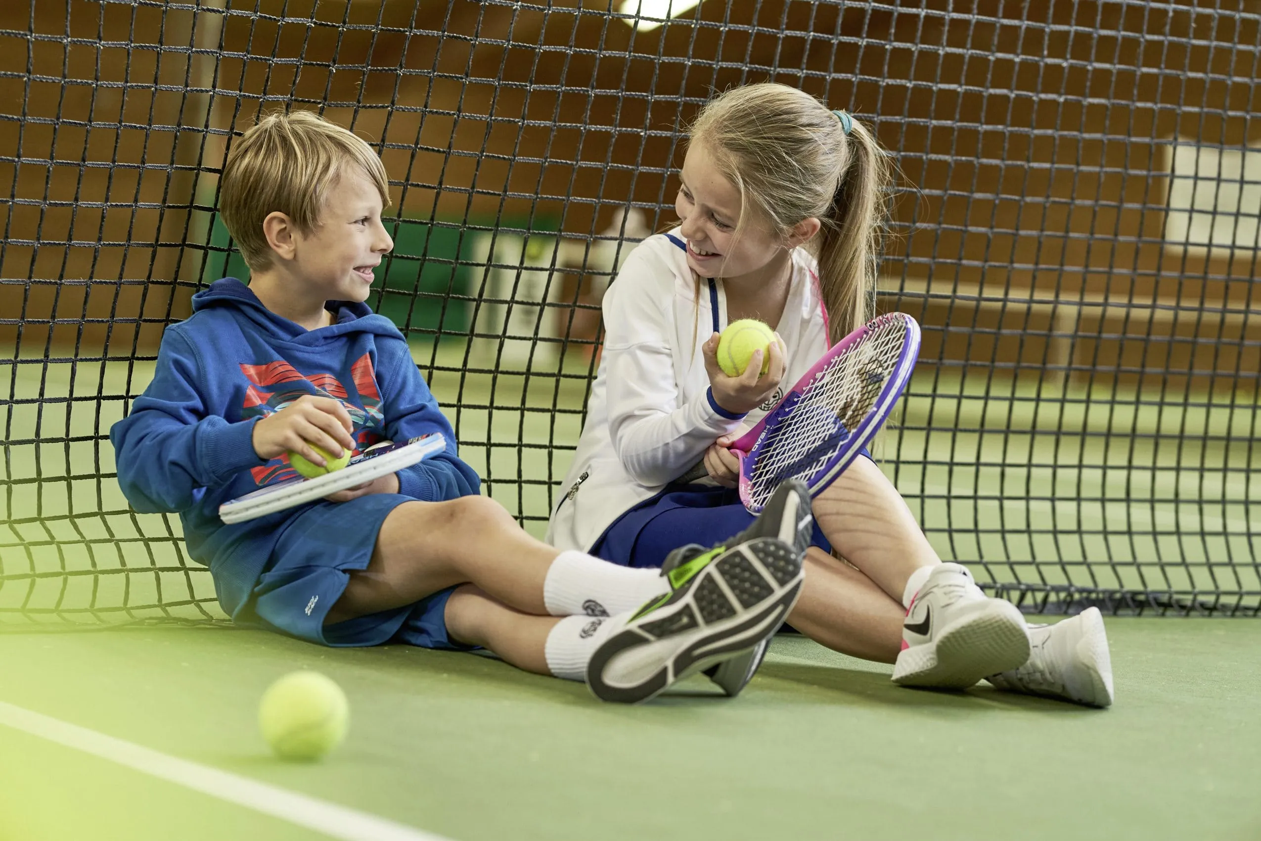 Zwei Kinder sitzen auf dem Indoor-Tennisplatz des Sporthotel Grafenwald