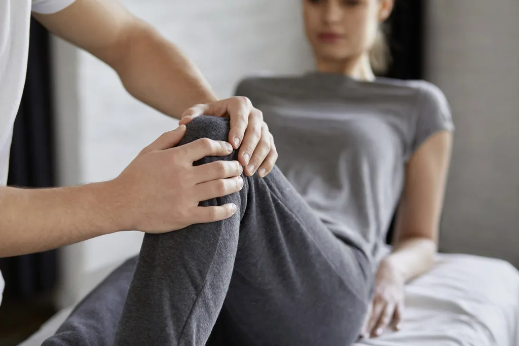 Eine Frau in einem grauen Joggingsanzug wird von einem Osteopahten am Knie behandelt