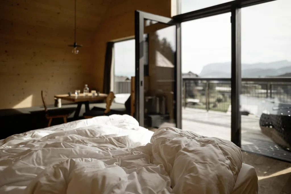 Zimmer mit ungemachtem, gemütlichem Bett und offener Balkontür im Naturhotel Pfösl