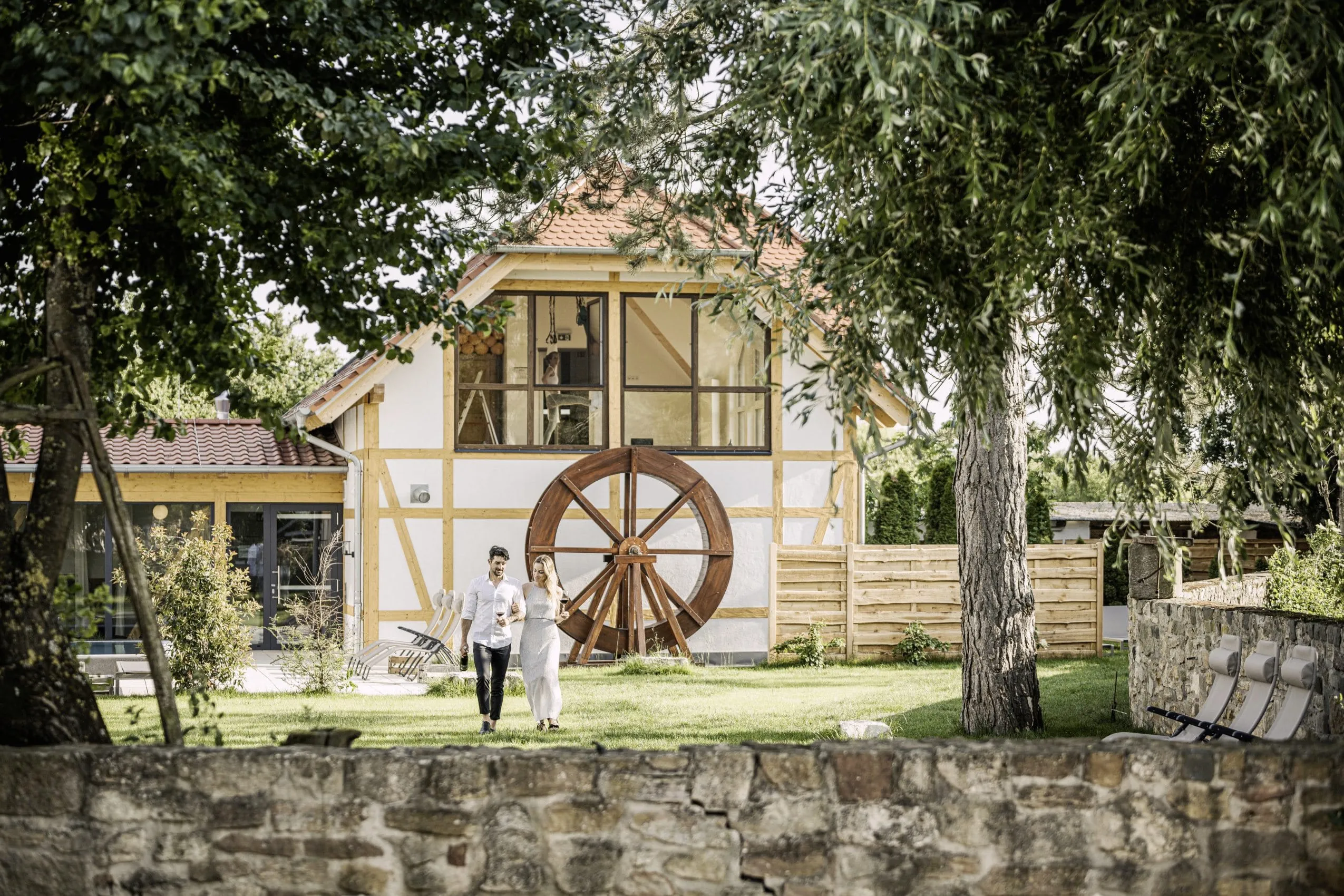 Junges Paar mit Weingl&auml;sern vor der historischen M&uuml;hle des Wellnesshotels Jordan&rsquo;s Unterm&uuml;hle