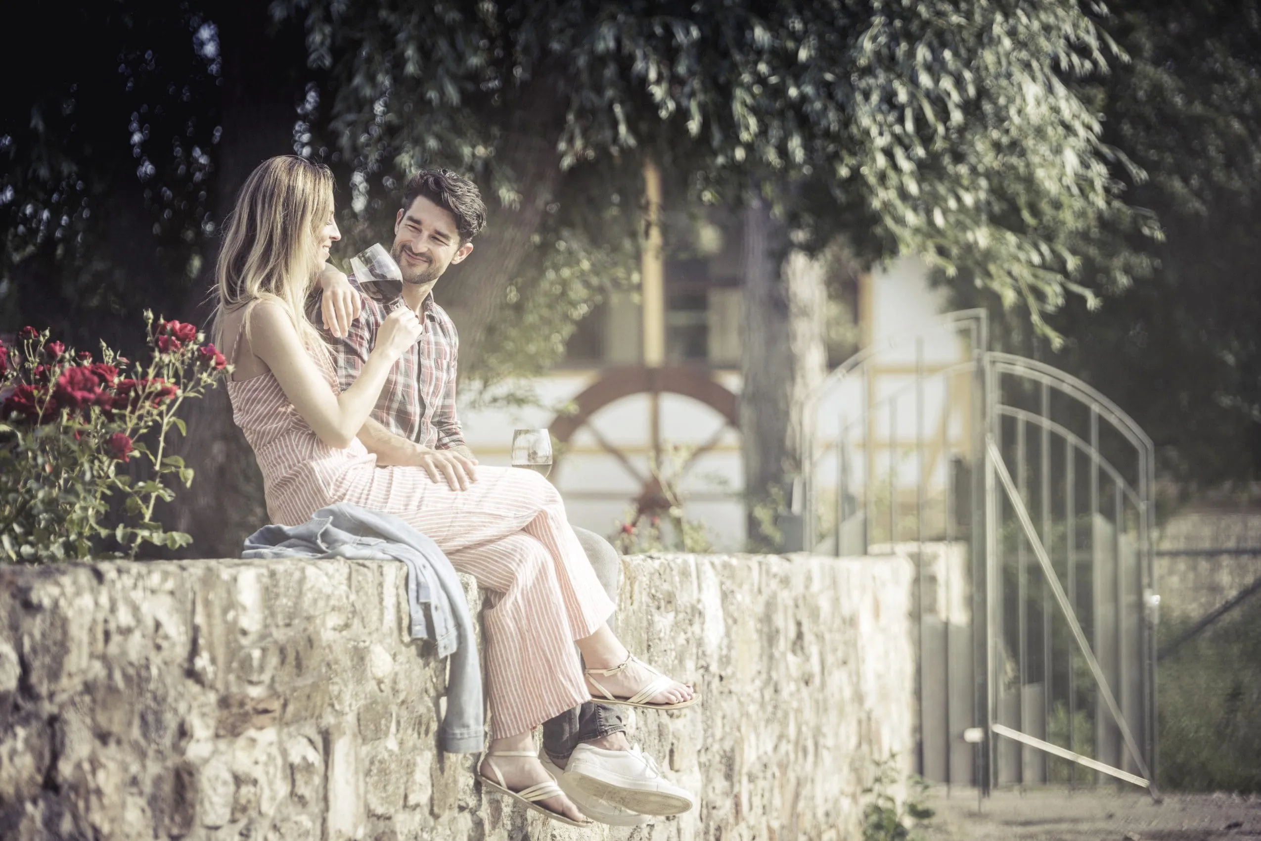 Ein P&auml;rchen sitzt auf der Mauer und trinkt Wein im Weinhotel Jordan&rsquo;s Unterm&uuml;hle