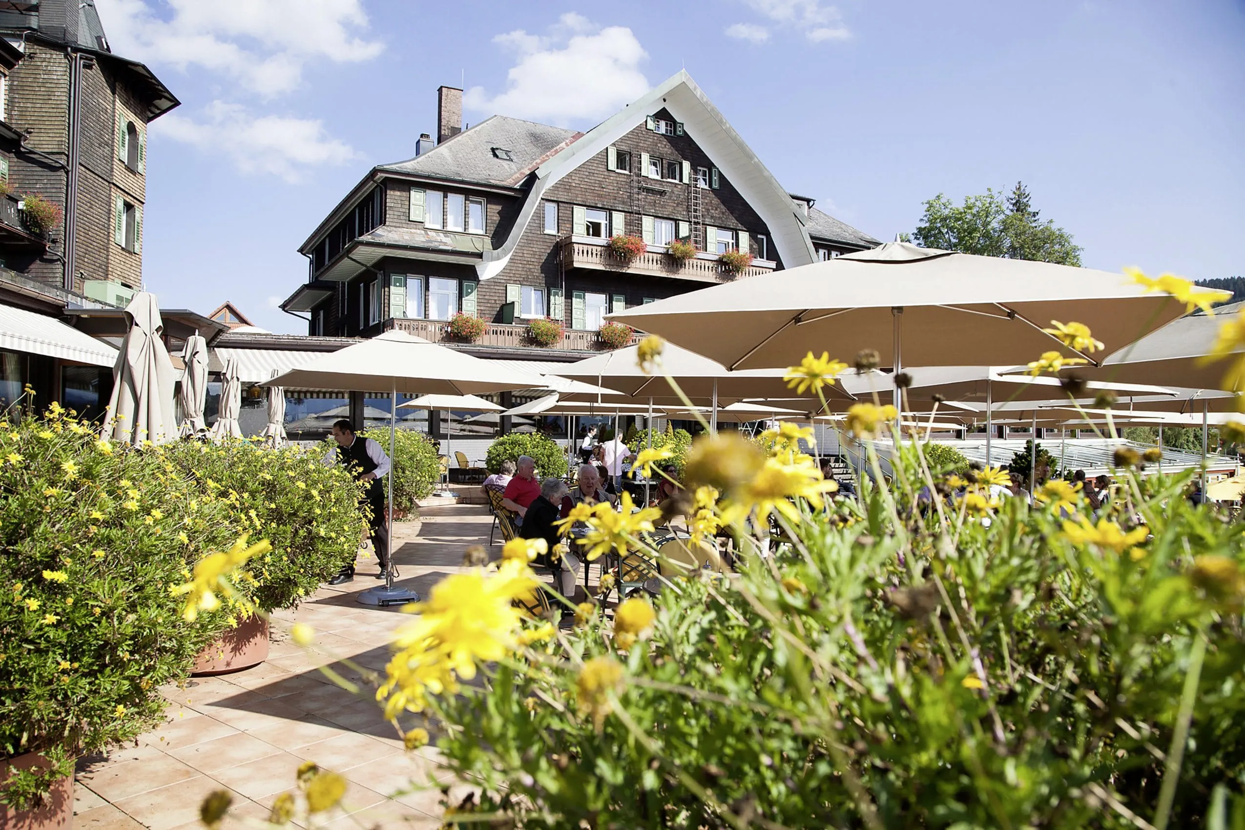 Blick auf das Hotelgeb&auml;ude des Treschers Schwarzwaldhotel am See mit Terrasse im Vordergrund