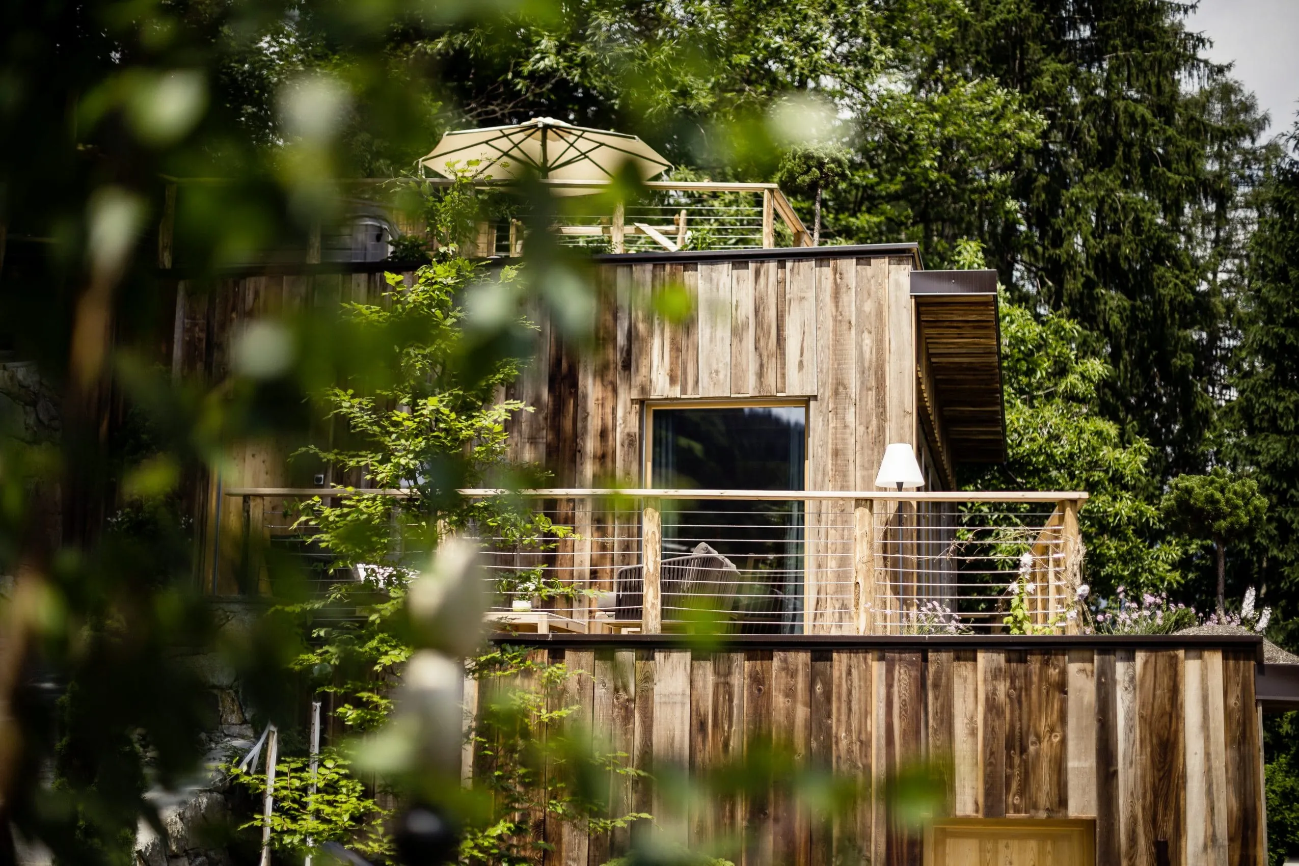 Blick auf die Holzfassade und Terrasse des Baumhaushotels Quellenhof Luxury Resort Passeier