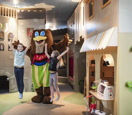 Zwei Kinder spielen mit Hotel-Maskottchen Falky im Kinderbereich des Familienhotels