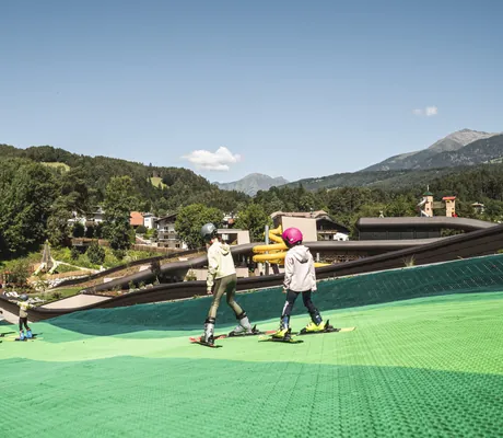 Zwei Kinder fahren im Sommer auf dem Dach des Falkensteiner Family Resort Lido Ski auf grünen Matten