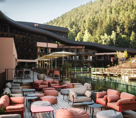 Gemütliche Outdoorterrasse des Falkensteiner Family Resort Lido mit gepolsterten Sitzmöbeln und Naturteich