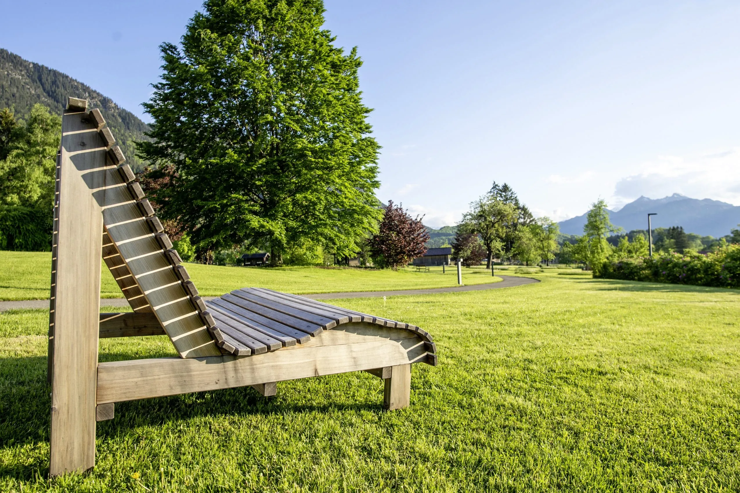 Gr&uuml;nanlage des Tagungshotels Alpenblick mit Holzbank und Blick auf die Berge