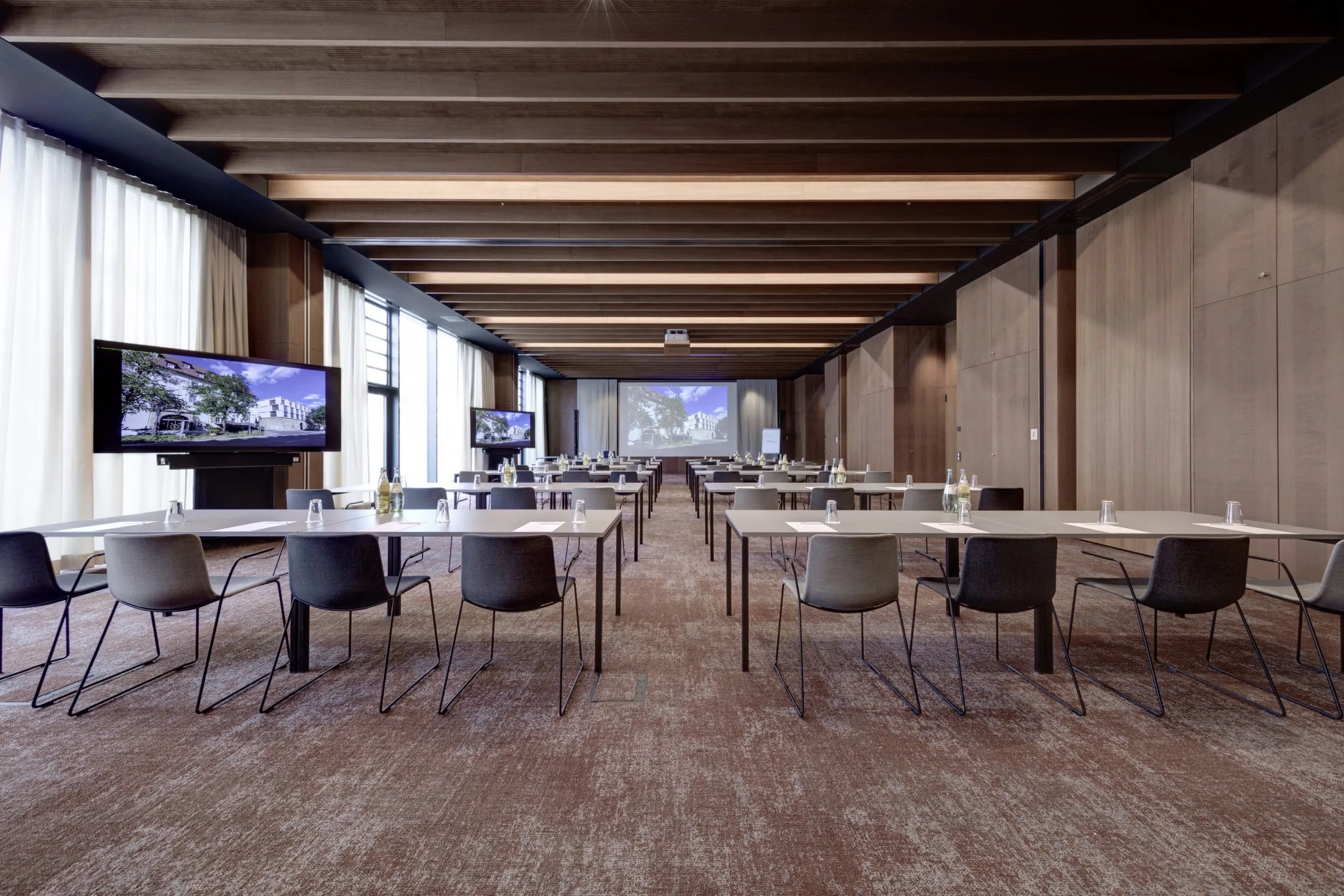 Tagungsraum mit mehreren Reihen an Tischen und Bildschirmen