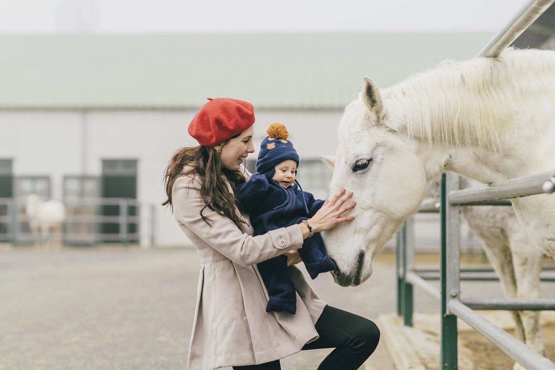 Mutter mit Baby im Arm streichelt wei&szlig;es Pferd im Reiters Finest Family Hotel