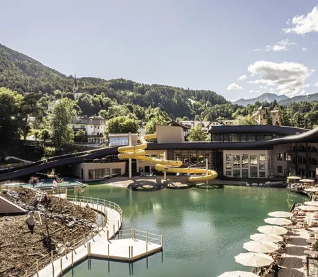 Hotelanlage außen mit See Wasserrutsche Terrasse und Ausblick auf Wald und Berge
