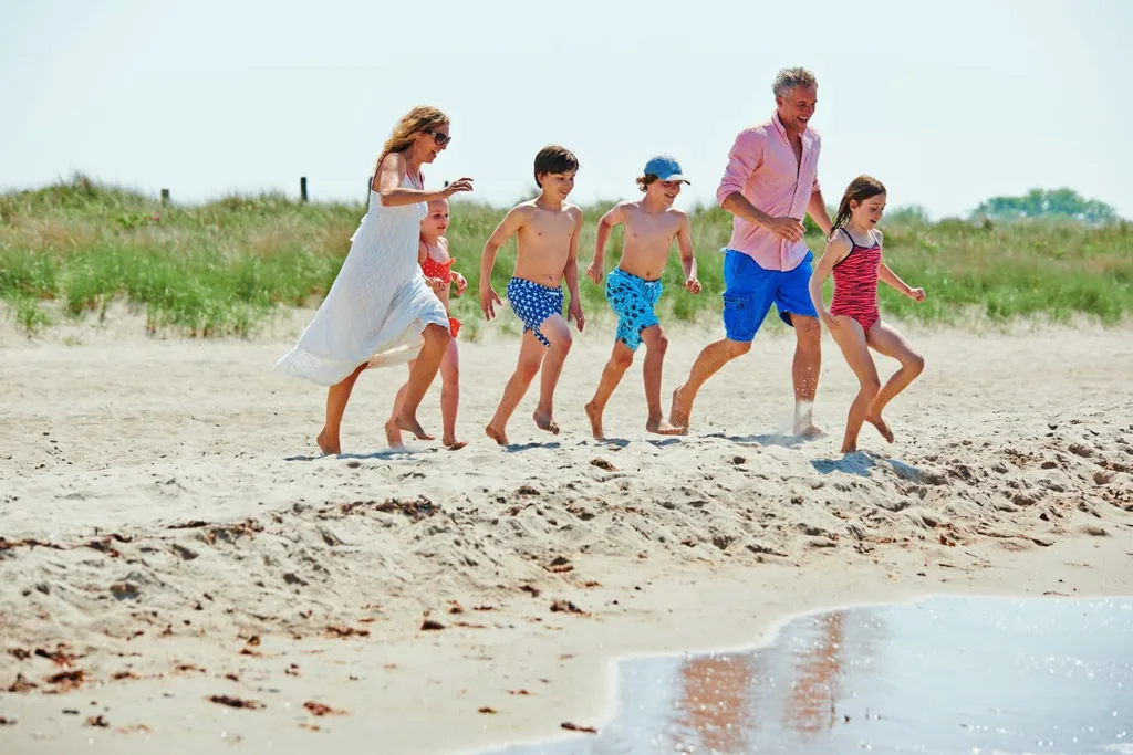 Familie mit Eltern und vier Kindern rennt auf Ostseestrand Richtung Meer