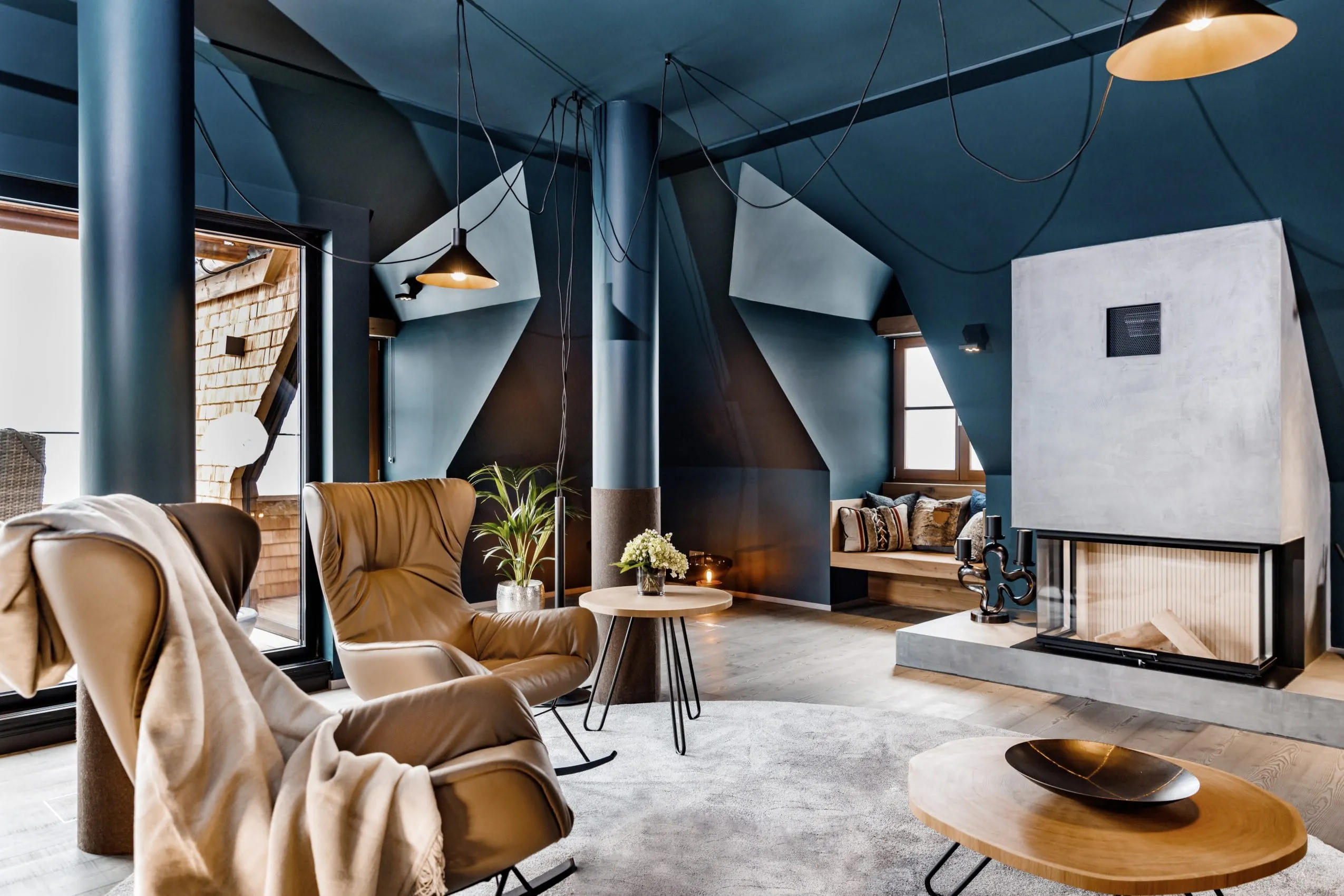 gro&szlig;z&uuml;gige Suite mit offenem Kamin, blauen W&auml;nden und Leder-Schaukelsesseln im A-ROSA Kitzb&uuml;hel