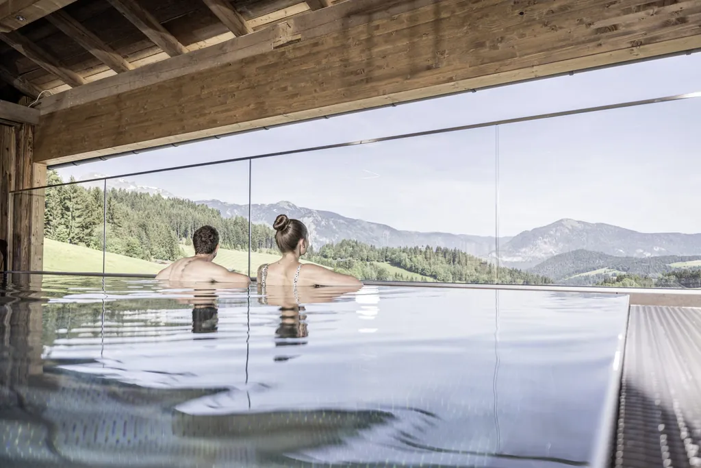 Paar in R&uuml;ckenansicht blickt auf Bergkulisse im Outdoor-Pool der Scheune der Hygna Chalets