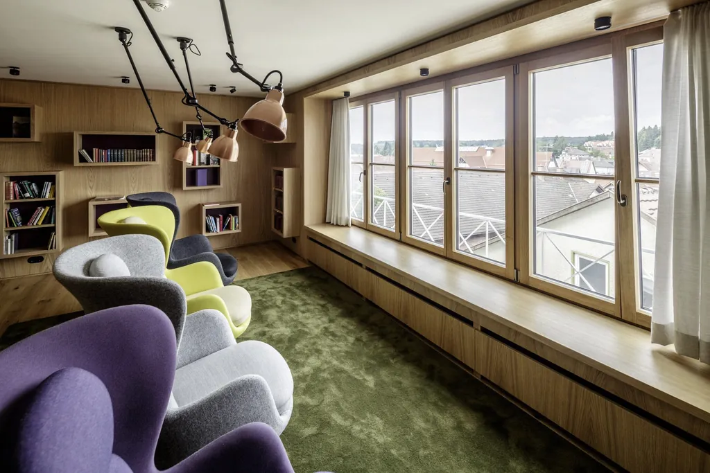 Bibliothek mit gr&uuml;nem Teppichboden, Deckenleuchten und Fensterblick &uuml;ber Dachlandschaft von Bad W&ouml;rishofen der KurOase im Kloster
