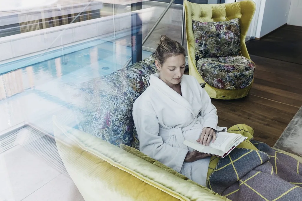 Lesende Frau im Bademantel auf farbiges Deignercouch im Livingroom Spa des Landhotel Vosh&ouml;vel