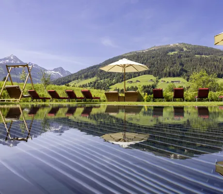 Outdoorpool mit roten Liegen am Rand und Blick auf die Berge im Alpbacherhof