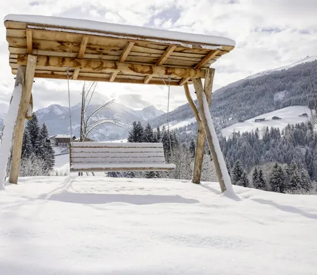 überdachte Holzhängeschaukel im verschneiten Garten des Alpbacherhof