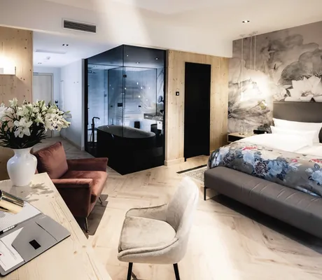 Zimmer mit verglastem Bad und Blumenvase mit Lilien im Hotel Bei Schumann