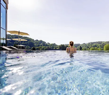 Frau im Badeanzug schaut aus dem Infinitypool im Pfalzblick Wald Spa Resort