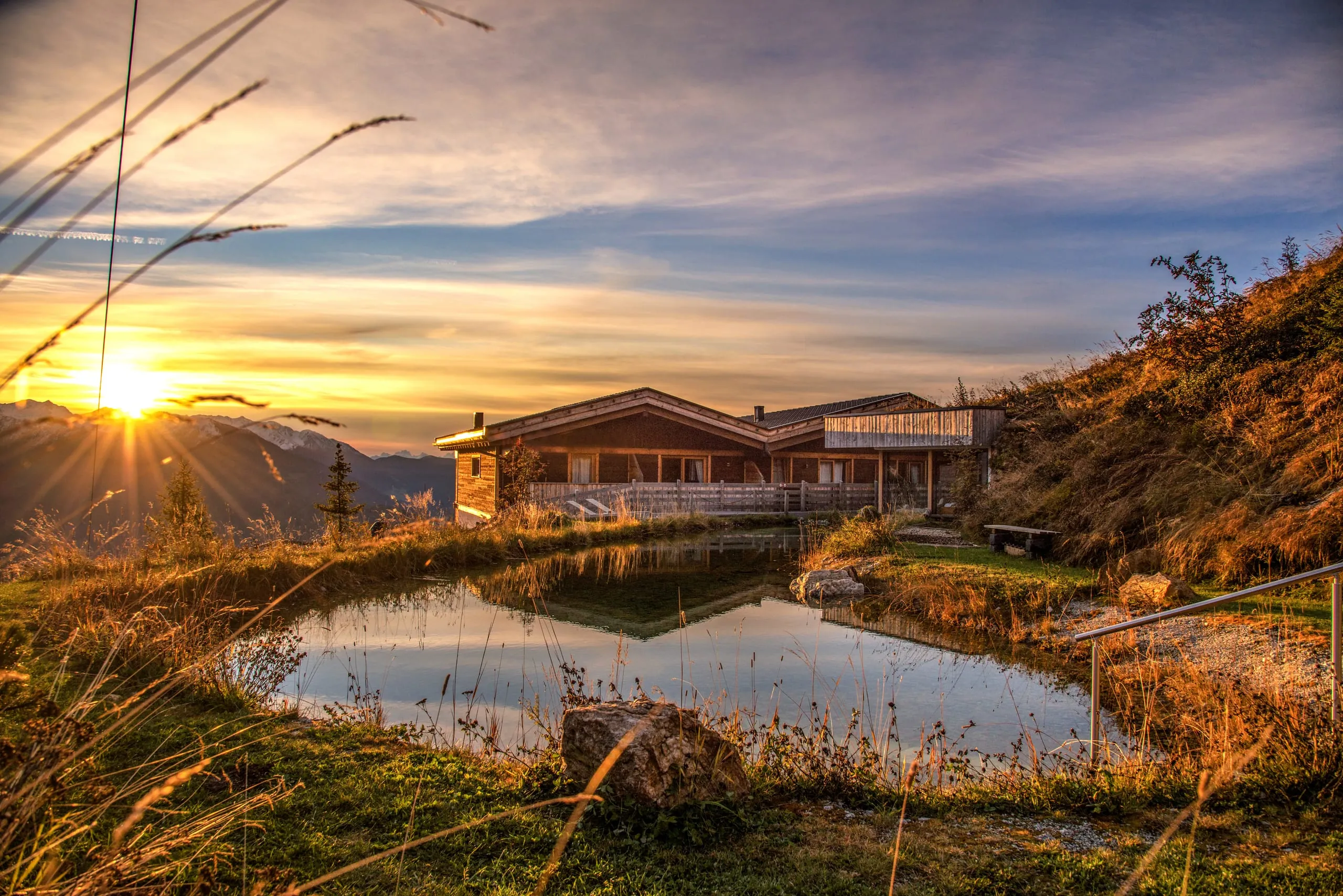 Blick auf das Chalet Stern auf dem Rosskopf bei Sonnenaufgang mit Naturbadeteich im Vordergrund