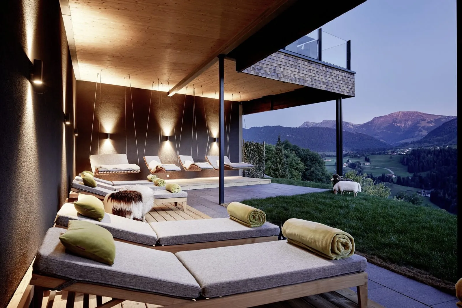 Gepolsterte Liegen und Schwebeliegen auf der Outdoorterrasse des Wellnesshotel Bergkristall mit Blick auf umgebende Landschaft in der D&auml;mmerung