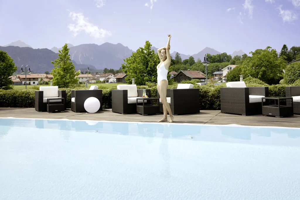 Frau steht im wei&szlig;en Badeanzug am Outdoorpool des Hotel Sommer mit Allg&auml;uer Alpen im Hintergrund