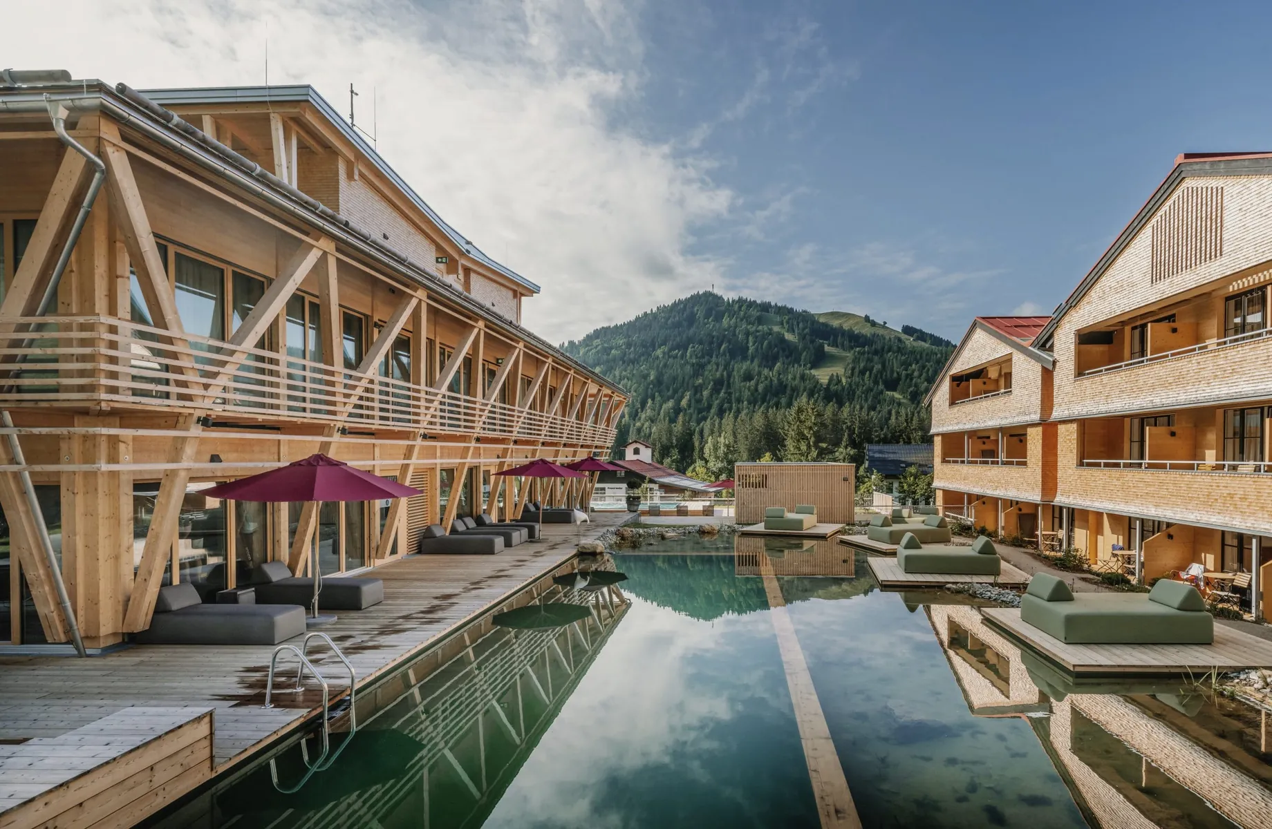 Blick auf den Naturbadeteich im Outdoor-Wellnessbereich des HUBERTUS Moutain Refugio Allgäu mit Ruheliegen