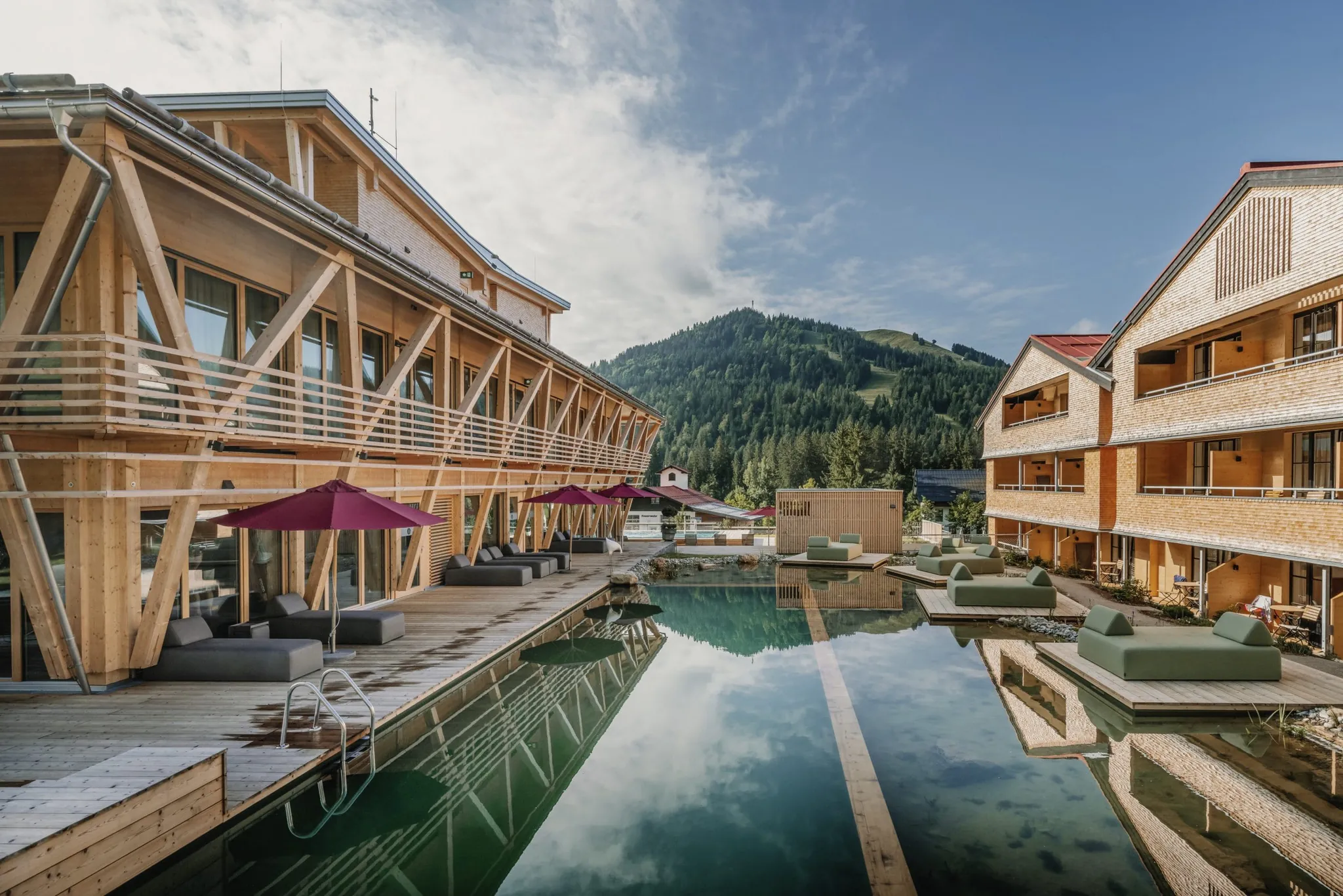 Blick auf den Naturbadeteich im Outdoor-Wellnessbereich des HUBERTUS Moutain Refugio Allgäu mit Ruheliegen