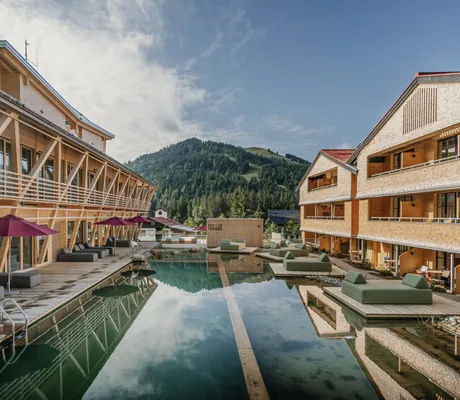 Blick auf den Naturbadeteich im Outdoor-Wellnessbereich des HUBERTUS Moutain Refugio Allgäu mit Ruheliegen