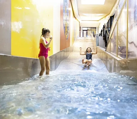 Mädchen rutscht auf der Indoor-Wasserrutsche während ein zweites Mädchen zuschaut im Familotel Sonnenpark