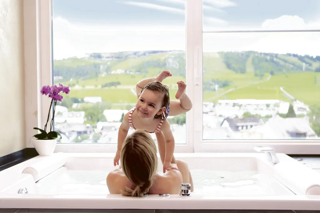 Frau hebt M&auml;dchen mit Badeanzug in der Badewanne &uuml;ber den Kopf im Sonnenpark Willingen