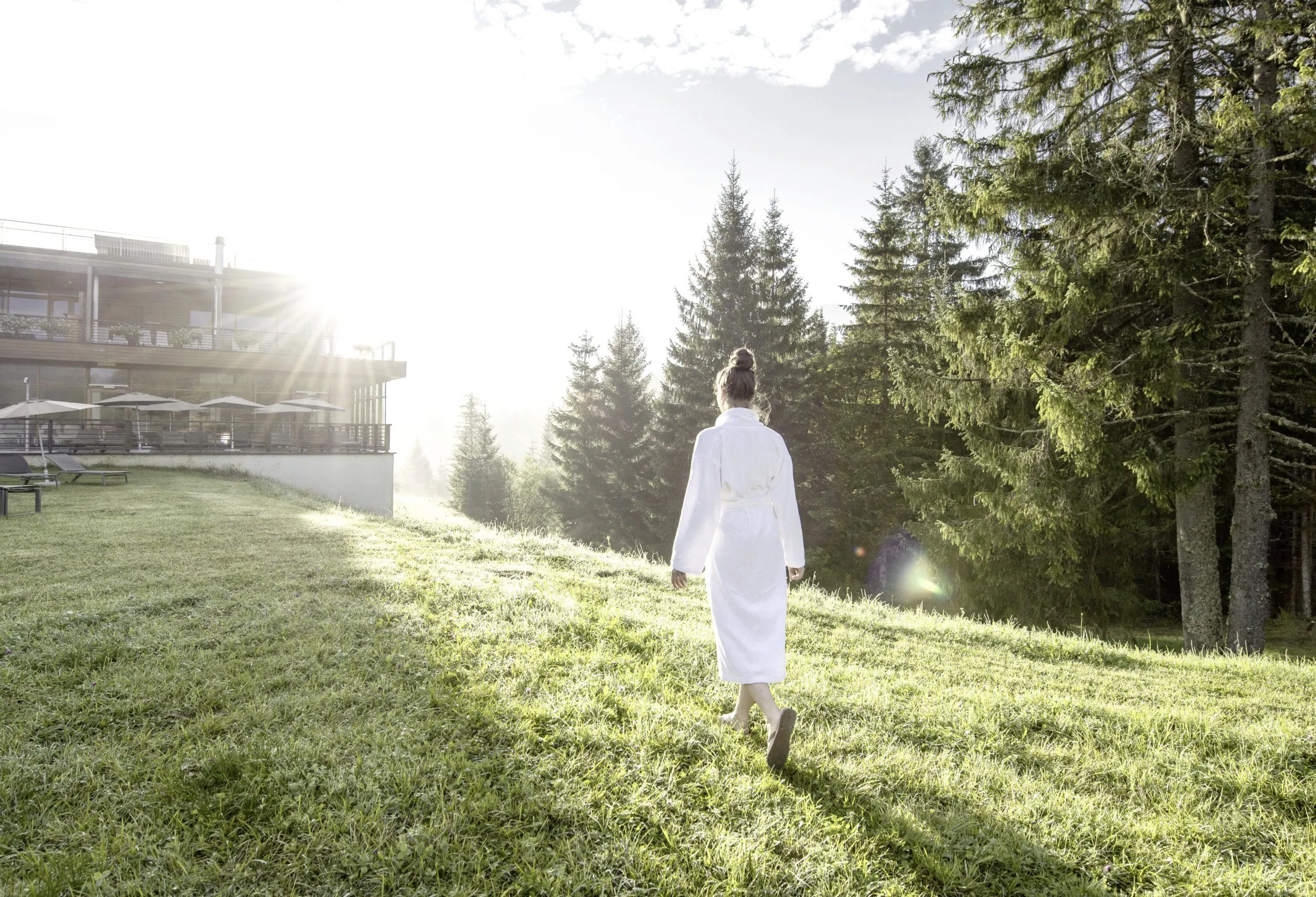 Frau geht im Morgengrauen im Bademantel &uuml;ber die Liegewiese des Luxus-Wellnesshotels Das Kranzbach Hotel & Wellnessrefugium