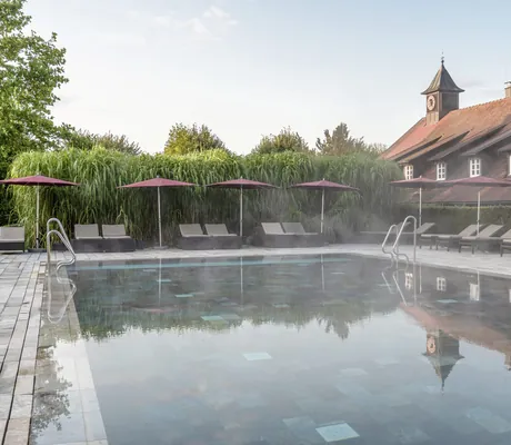 Outdoorpool mit aufgespannten roten Sonnenschirmen am Beckenrand im Wald- & Schlosshotel Friedrichsruhe