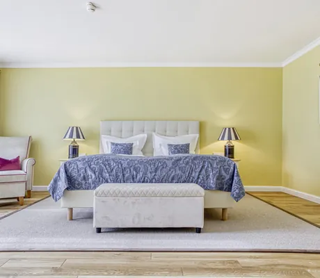 großzügiges gelb gestrichenes Doppelzimmer mit blauem Bettüberwurf im Wald- & Schlosshotel Friedrichsruhe