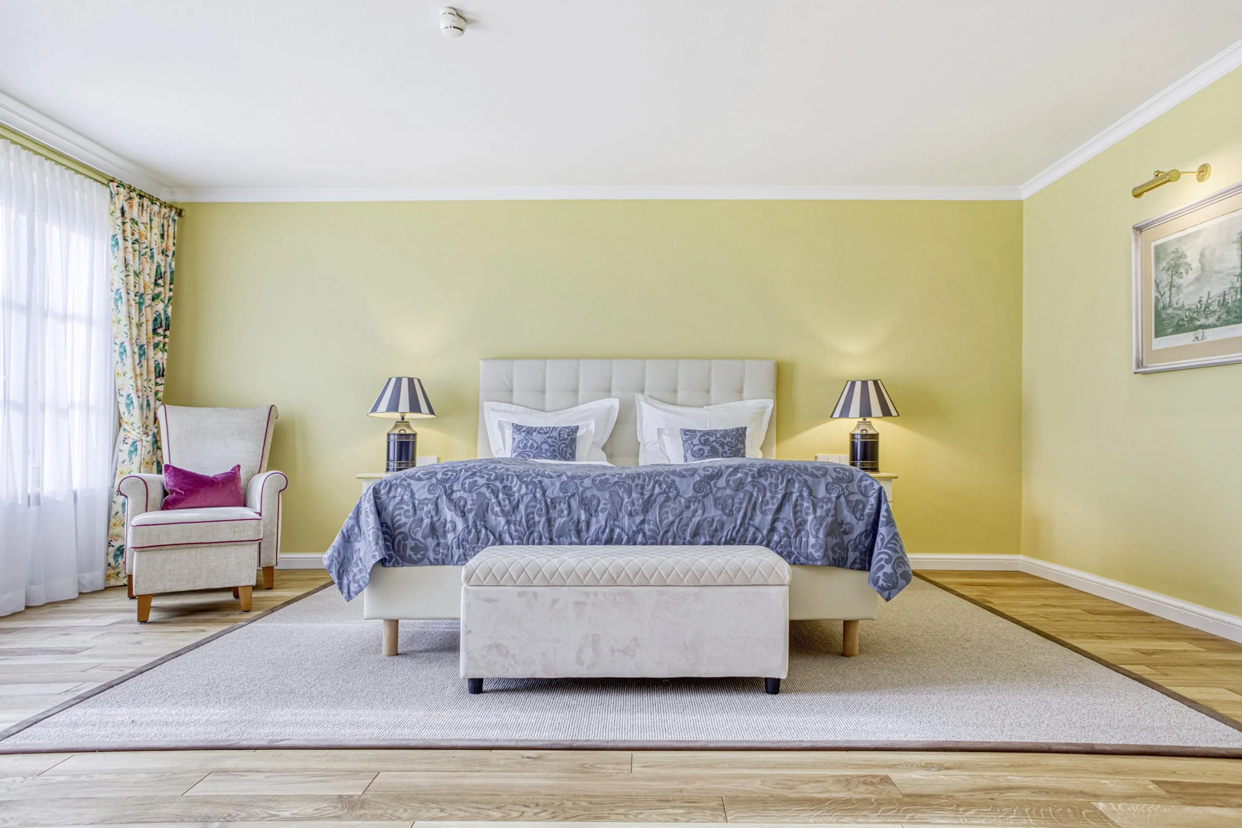 gro&szlig;z&uuml;giges gelb gestrichenes Doppelzimmer mit blauem Bett&uuml;berwurf im Wald- & Schlosshotel Friedrichsruhe