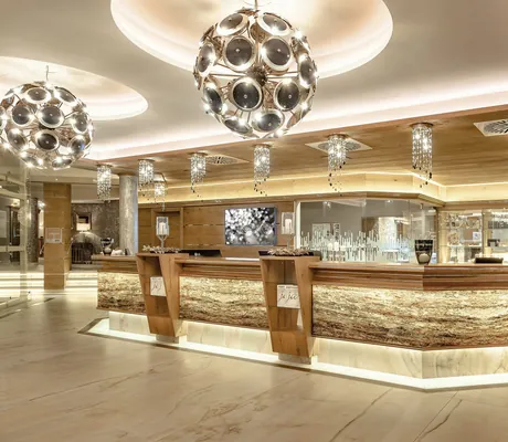 golden beleuchtete Spa-Rezeption mit zwei großen futuristischen Hängeleuchten im Wellnesshotel Jagdhof Röhrnbach
