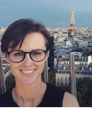 Autorenporträt Anna Rockenfeller mit Brille und Top in Paris vor Stadtkulisse mit Eiffelturm