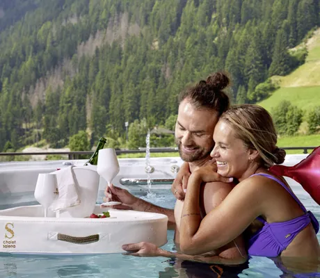 Pärchen im Whirlpool des Chalet Salena mit Herz-Luftballon und schwimmendem Sekt-Tablett