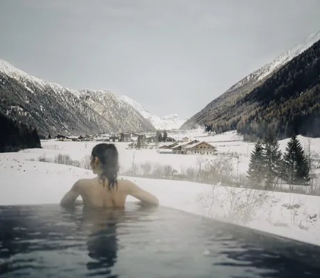 Junge Frau steht im Winter am Rande des beheizten Outdoor-Infinitypools der Südtirol Chalets Valsegg und blickt das Tal entlang