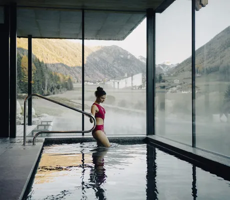 Junge Frau im roten Badeanzug steigt in den Indoorpool der Südtirol Chalets Valsegg