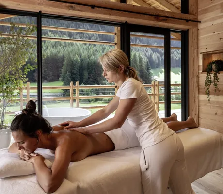 Junge Frau liegt auf einer Massageliege in den Südtirol Chalets Valsegg und erhält eine Rückenmassage